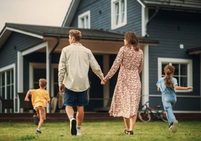 young beautiful couple walking outdoors towards the country house, holding hands. their little son and daughter running together with them. young modern family at home, footage from the back.